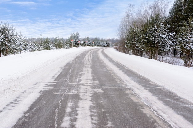 Patterns on the winter highway in the form of four straight lines. Snowy road on the background of snow-covered forest. Winter landscape.