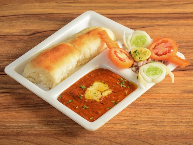 Pav bhaji is a fast food dish from india thick and spicy\
vegetable curry served with a soft bread roll or bun paav and\
butter isolated over a rustic wooden background selective\
focus