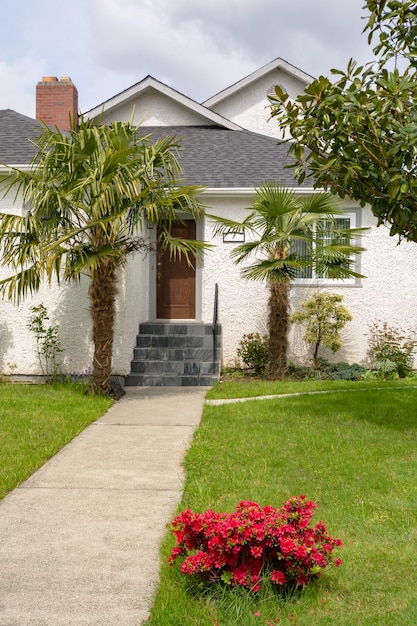 Paved pathway to the house entrance over front yard decorated with red flowers