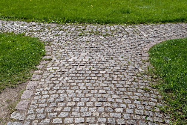 Foto pavimentata con pietre grezze squadrate, la strada si divide in due direzioni tra l'erba verde