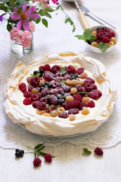 Pavlova cake met room en bessen en een boeket bloemen op een lichte achtergrond. rustieke stijl, selectieve aandacht.