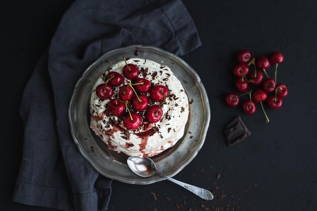 Pavlova cake with fresh cherry cheese cream and chocolate chips in vintage silver plate over dark grunge background top view