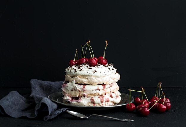 Торт Павлова со свежим кремом из вишневого сыра и шоколадной стружкой в винтажной серебряной тарелке на темном гранж-фоне