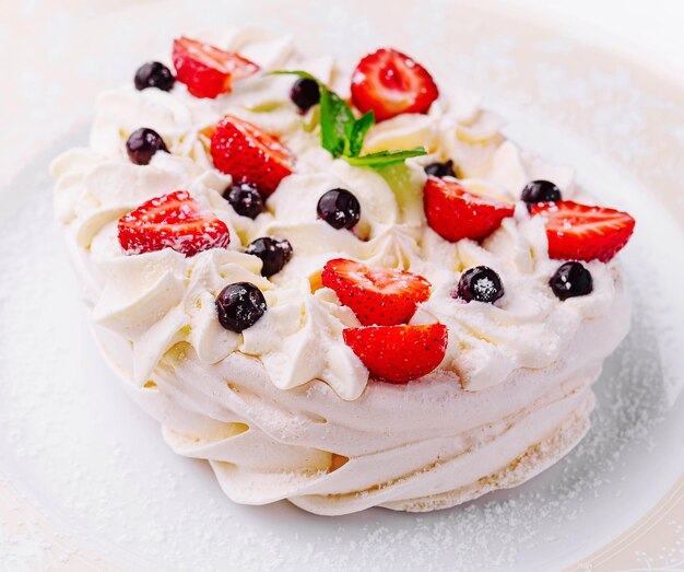 Pavlova-koekjes met room en verse bessen op het bord