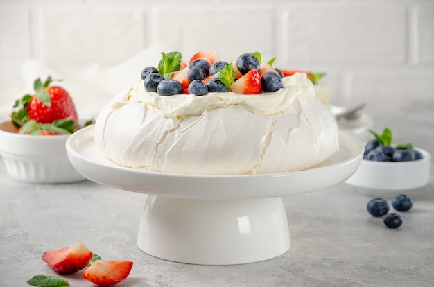 Торт безе "Павлова" со взбитыми сливками и свежими ягодами сверху на тарелке на сером фоне бетона.