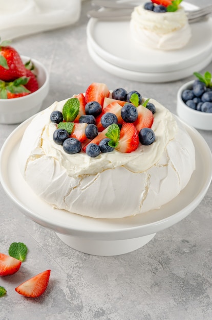 Pavlova meringue cake with whipped cream and fresh berries on top on a white plate