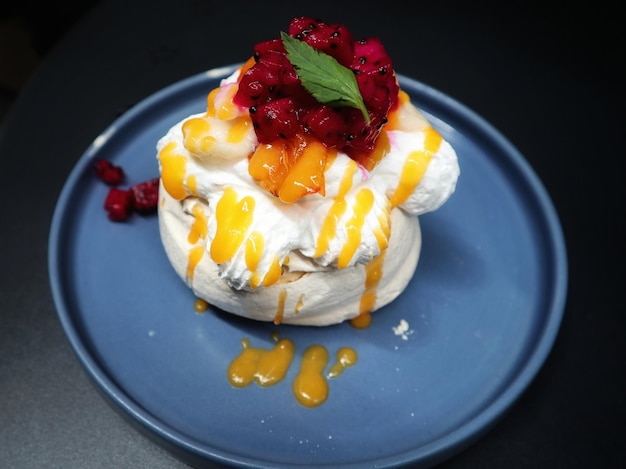 Pavlova serve in a blue plate a meringue dessert usually topped with strawberry and orange fruit and whipped cream