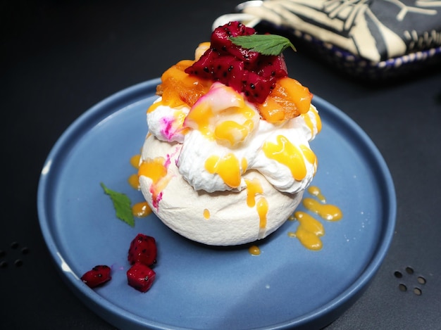 Pavlova serve in a blue plate a meringue dessert usually topped with strawberry and orange fruit and whipped cream