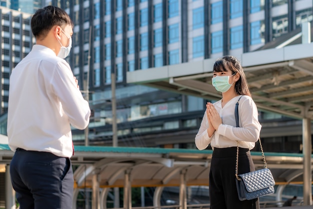 Pay respect is new novel greeting to avoid the spread of coronavirus Two Asian young businessman and businesswoman friends meet in font of office building.