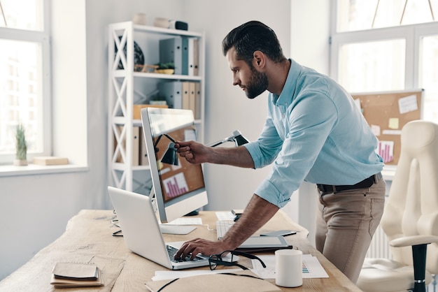 Prestando attenzione ad ogni dettaglio. giovane uomo d'affari moderno che analizza i dati utilizzando il computer mentre si lavora in ufficio