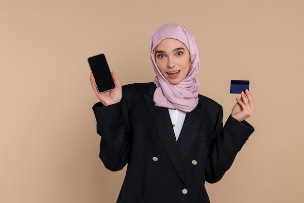 クレジットカードでピンクのヒジャブを着た可愛い女性を笑顔でオンラインで支払います