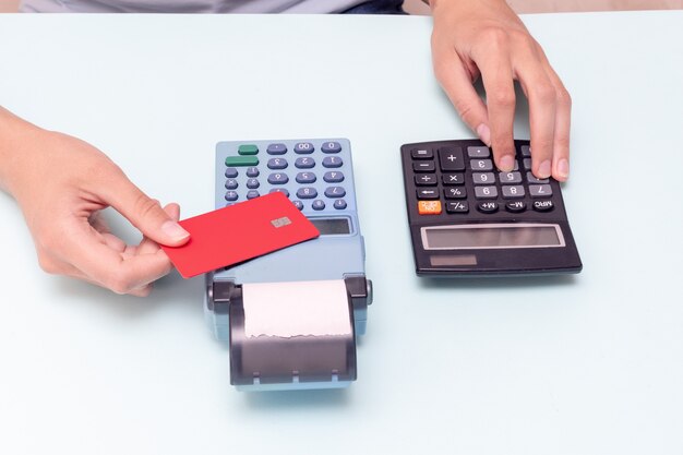 Payment for purchases by credit card. Holding a credit card over the cash register and calculating the cost of a purchase on a calculator on a blue background. Black Friday concept