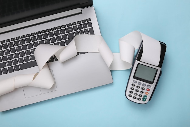 Payment terminal with cash tape and laptop on blue background Payment for purchases Online shopping Top view