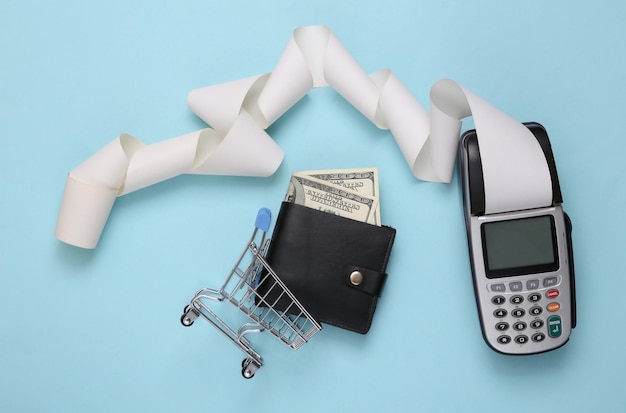 Photo payment terminal with cash tape and mini shopping trolley with purse on blue background shopping concept top view