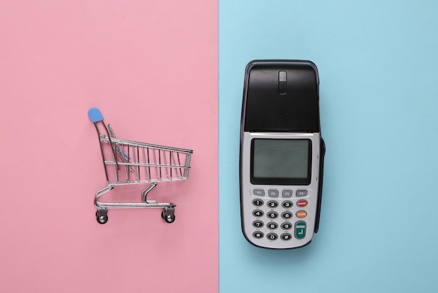 Фото Платежный терминал с мини-тележкой для покупок на синем розовом фоне концепция покупок вид сверху