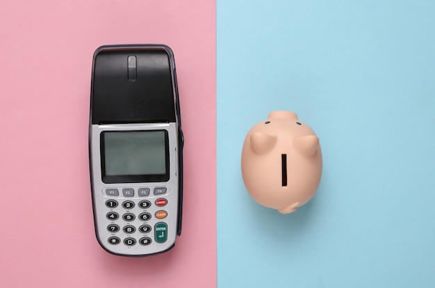 Payment terminal with piggy bank on blue pink background Save money concept Top view