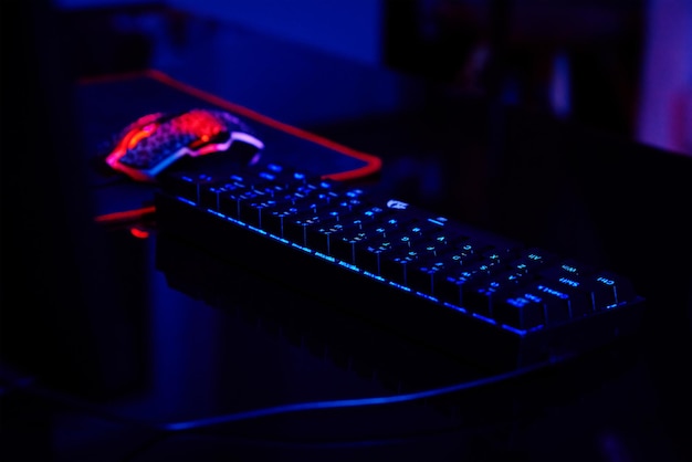 PC with rgb keyboard for gaming computer video games with neon colored background, dark room with game workplace without people