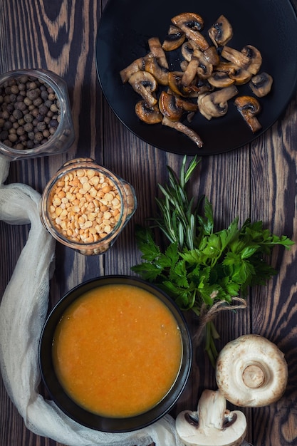 Pea soup in black plate Fried mushrooms Dried pea pepper in glass jars Fresh parsley and rosemary Dark wooden table Toned