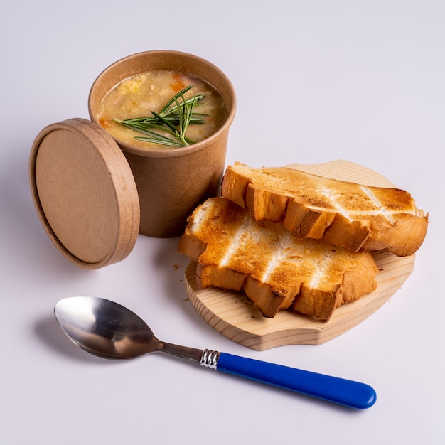 紙の使い捨てカップにエンドウ豆のスープ、テイクアウト、または青色の背景にパンと食品の配達