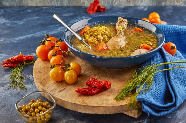 Pea soup with chicken, carrots, tomatoes and herbs in a deep plate on wooden board with napkin.