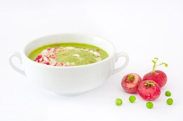 Pea soup with radishes in white bowl isolated