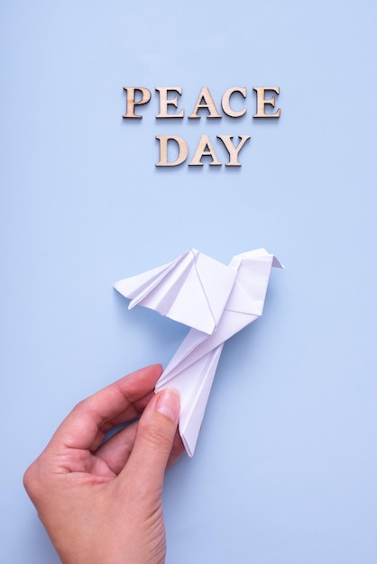 peace day text from wooden letters with white paper dove in female hand on blue background international peace day concept vertical photo