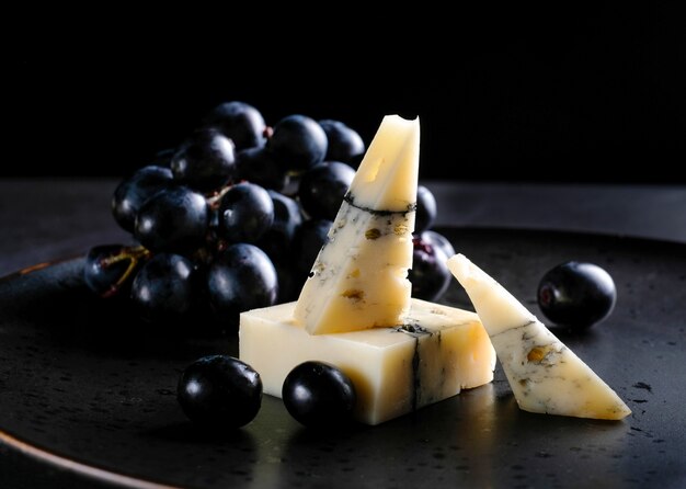 Peace of handmade cheese on plate with grapes, nuts and honey at black table. Close up.