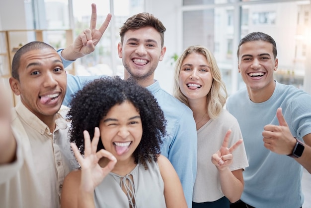 Peace sign thumbs up and selfie of business people in office Comic face portrait or group of friends or workers with tongue out and hand gestures taking pictures for social media or happy memory