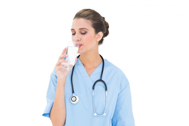 Peaceful brown haired nurse in blue scrubs drinking milk