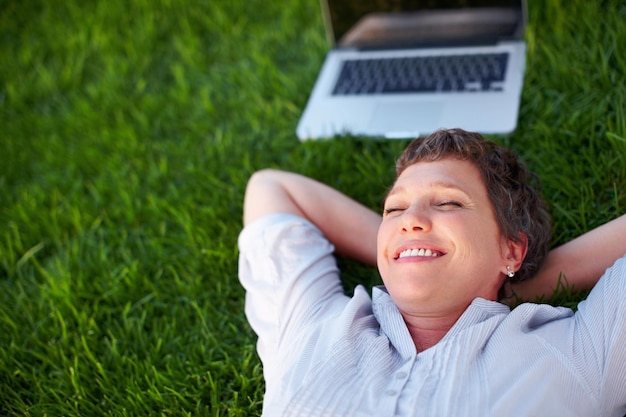 Peaceful fantasy Relaxed mature woman with laptop smiling while lying on grass