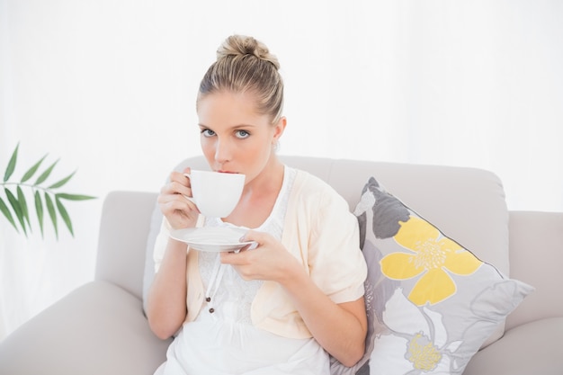 Peaceful fresh model drinking coffee sitting on sofa