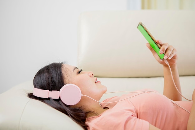 Peaceful girl in modern wireless headphones sit relax on comfortable couch listening to music