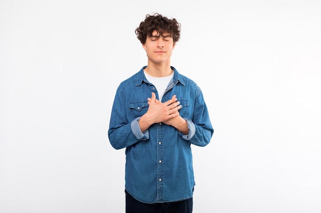 Peaceful guy pressing hands to chest making wish white background