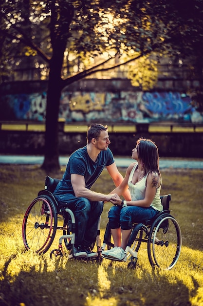 Peaceful handicapped young couple on two wheelchairs in autumn park.