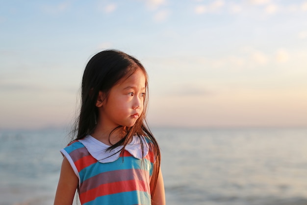 Peaceful little child girl standing on beach at sunset light with looking out.