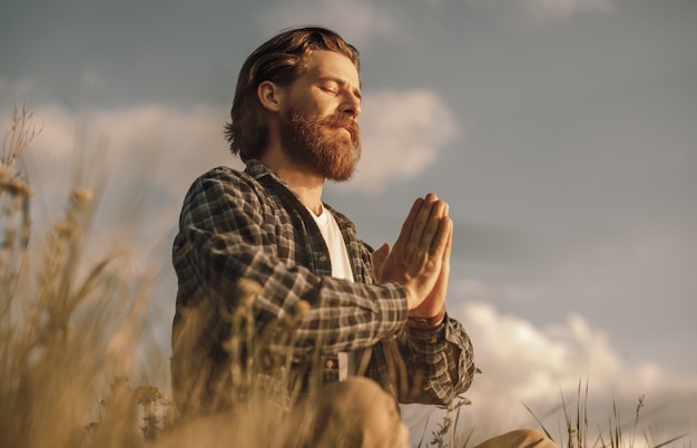 Peaceful male sitting in lotus pose in field and meditating