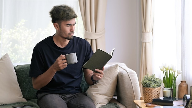 コーヒーを飲み、自宅のソファで本を読んで平和なミレニアル世代の男