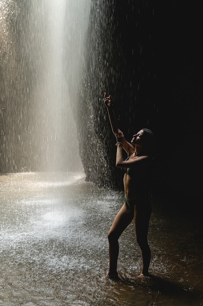 Peaceful place. Tender fitness girl raising her arm while touching water and posing on camera