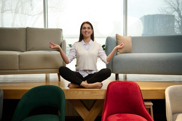 Peaceful relaxed middleaged beautiful woman seller in a furniture store sits in a lotus position and meditates The concept of tranquility and a clientoriented approach