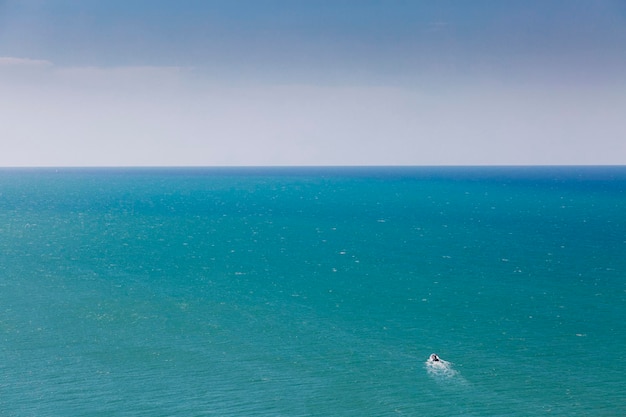 The peaceful sea meets the clear blue sky on a neverending horizon with a tiny white boat sailing