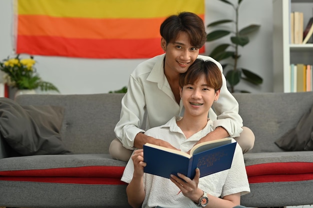 写真 平和な 2 人の若い男性の恋人がお互いを抱きしめて、居心地の良いリビング ルームで本を読む同性愛者と愛のコンセプト