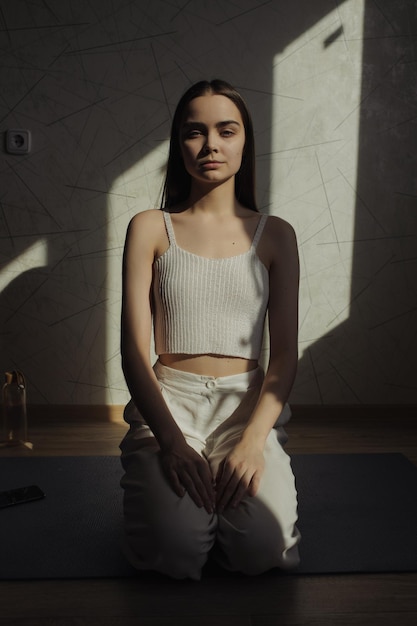 Peaceful woman in white clothes sitting in Vajrasana or Thunderbolt pose and doing yoga on mat