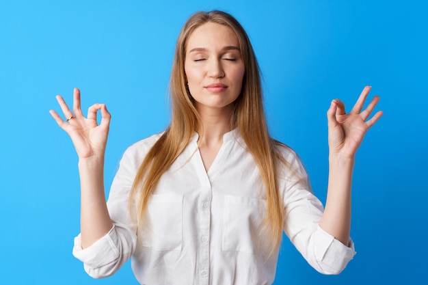 Peaceful young blonde woman portrait in zen pose against blue background