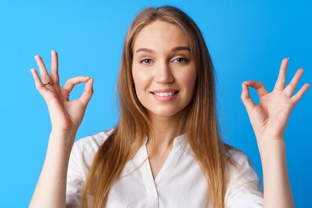 Peaceful young blonde woman portrait in zen pose against blue background