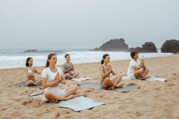 Peaceful young men and women meditating together on beach practicing yoga in lotus position with