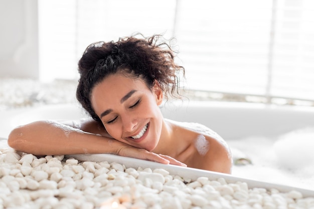 Giovane donna pacifica che si rilassa nel bagno caldo di bolle che si rilassa nell'acqua calda con gli occhi chiusi godendo