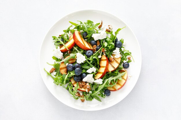 Peach blueberry and arugula fresh fruit salad with cheese and almond nuts top view