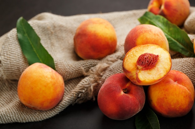 Peach fruit on a black background with a cloth of burlap and green leaves. Sweet and juicy peach slices with a stone