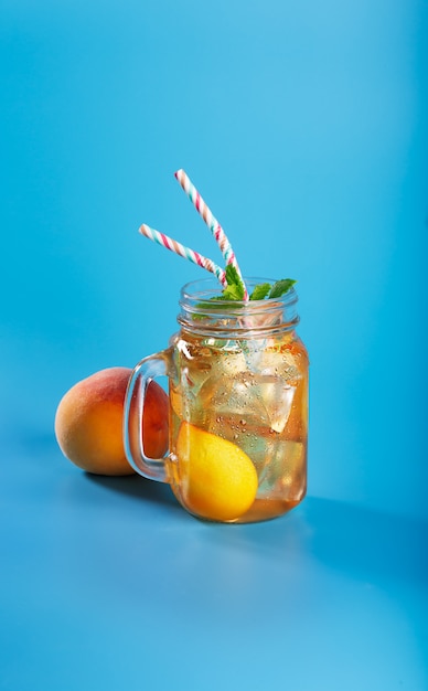 Peach ice tea on blue background with mint and ice, nice drink for summer hot season