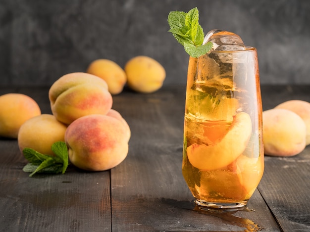 Peach ice tea with mint and ice on a dark wooden background.
